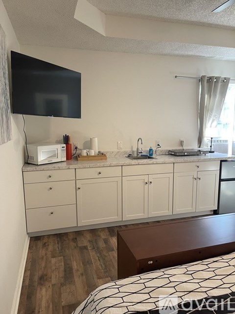 A kitchen with white cabinets and a black TV mounted on the wall.