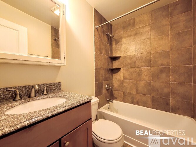 A bathroom with a brown tiled shower area and a white toilet.
