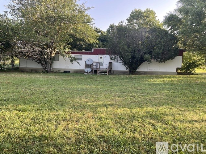 A white house with a red roof is surrounded by trees and grass.