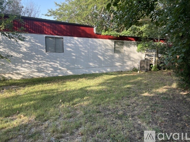 A white building with a red roof is surrounded by greenery.