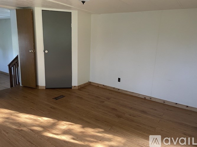 A room with a wooden floor and a white wall with a door.