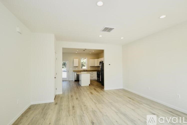 A spacious room with wooden flooring and a kitchen area in the background.