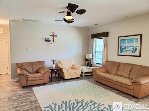 A living room with a ceiling fan, two leather chairs, a sofa, and a painting on the wall.