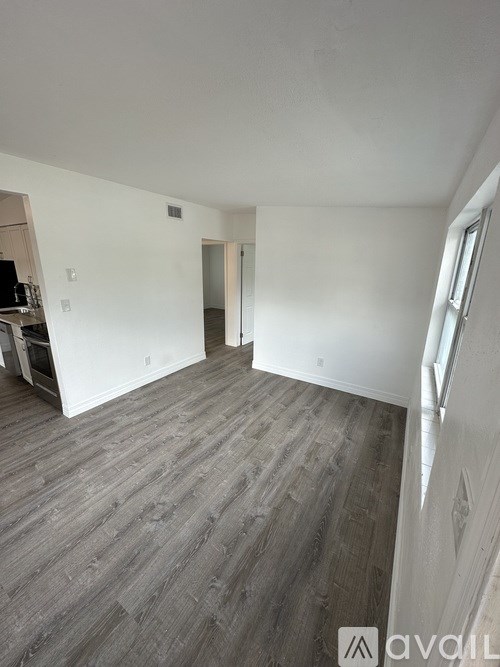 A room with wooden flooring and white walls, with a doorway leading to another room.