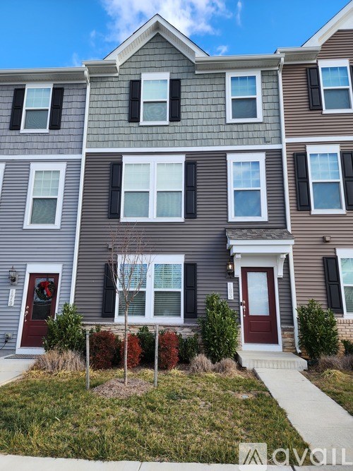 A grey two story house with a red door and a tree in front.