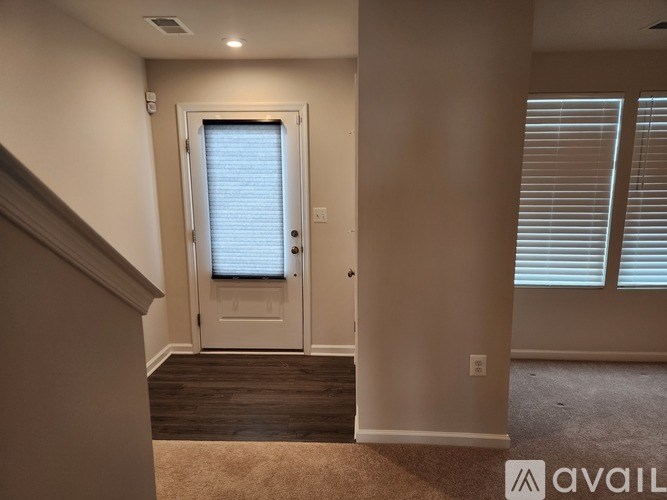 A hallway with a carpeted floor, a door with blinds, and a wall with a switch.