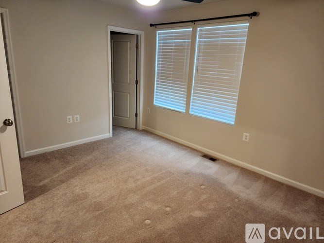 A room with a carpeted floor, a door, and a window with blinds.