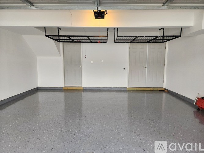 A spacious room with a grey floor and white walls, featuring a black metal pipe ceiling structure and two white doors.