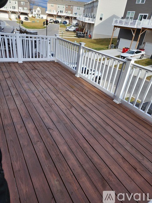 A wooden deck with a white railing and a building in the background.