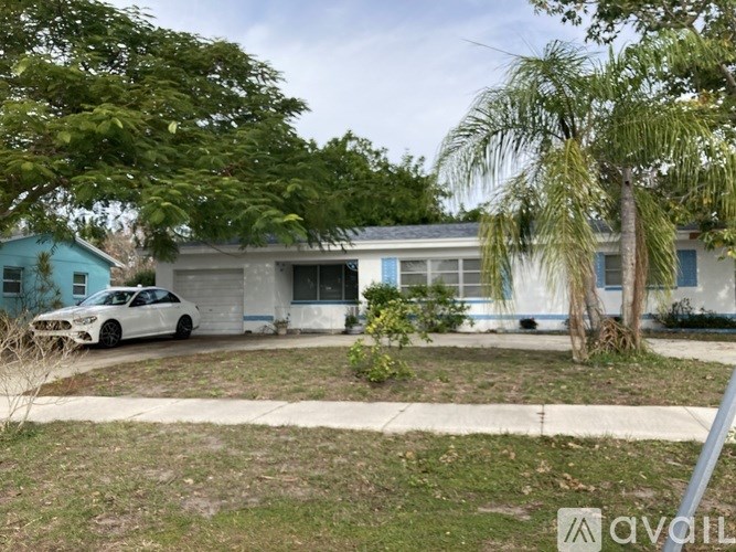 A white car is parked in front of a blue house.