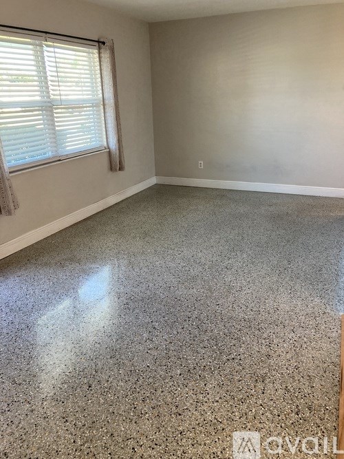 A room with a grey floor and a window with blinds.