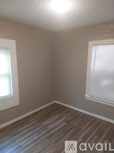 A room with wooden flooring and two windows.