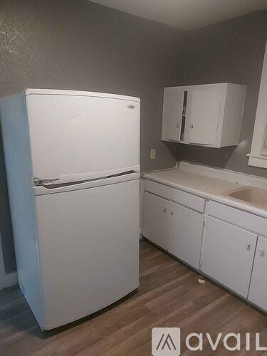 A white refrigerator is in a kitchen with white cabinets.