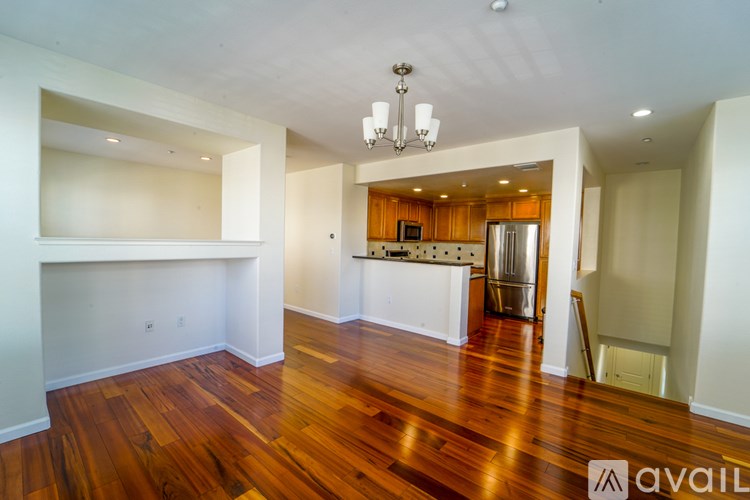 A large empty room with wooden floors and a kitchen area in the background.