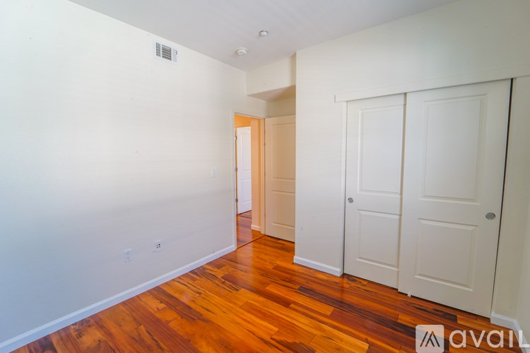 A room with wooden floors and white walls with a door in the distance.