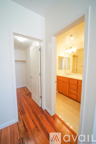 A hallway with a wooden floor leads to a bathroom.