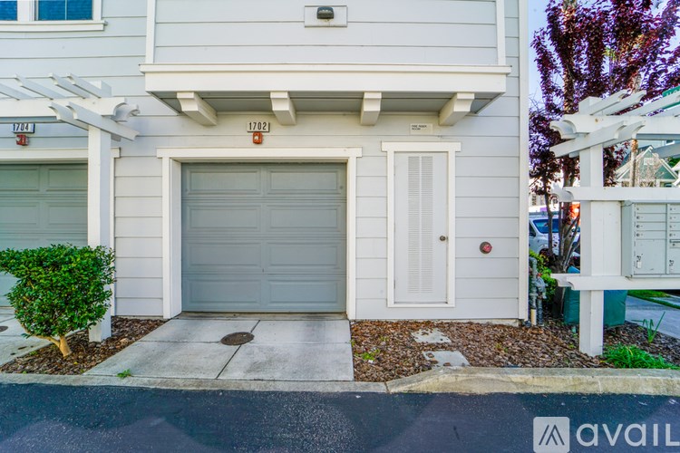 A white house with a garage door and a small tree in front.