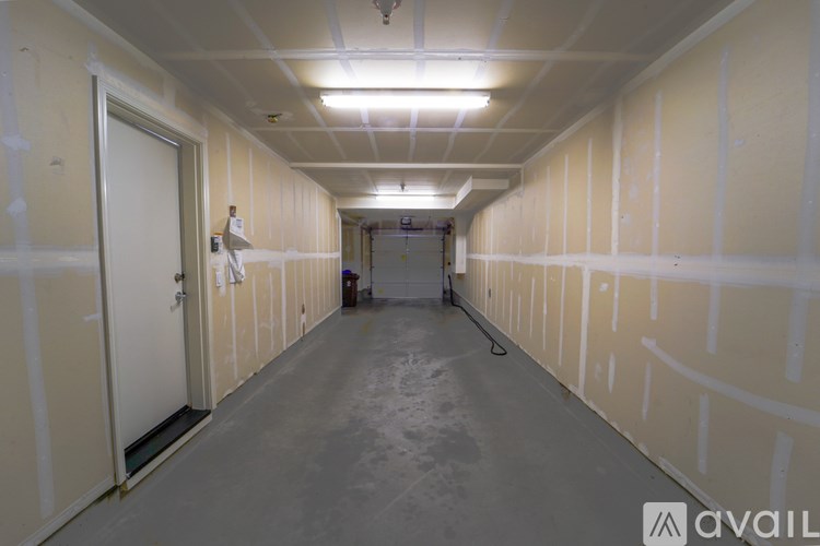 A long, empty hallway with white walls and ceiling, and a door on the left side.