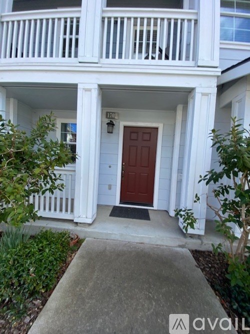 A white house with a red door and a black mat on the concrete walkway.