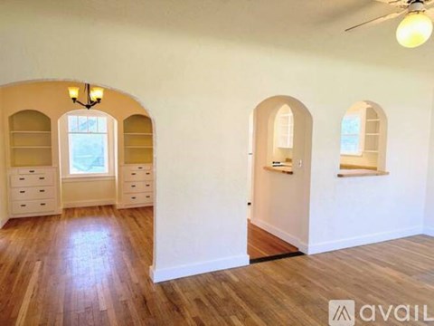 A room with wooden floors and arched windows with a sign that says "available".