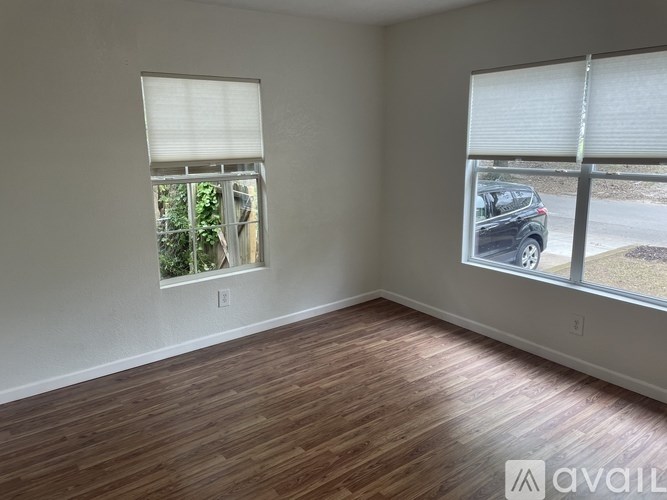 A room with wooden flooring and two windows with blinds.