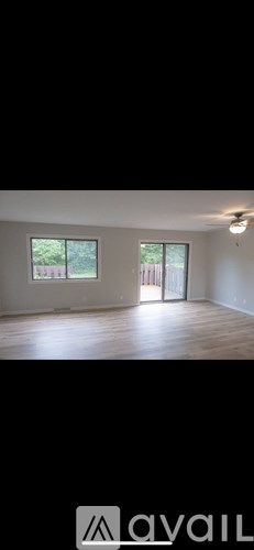 A room with wooden flooring and a window overlooking a fence.