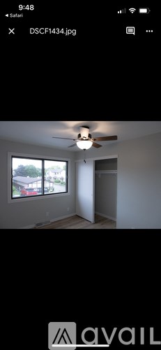A room with a ceiling fan and a window overlooking a house.