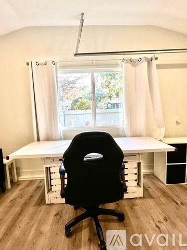 A black office chair is in front of a white desk with a window behind it.