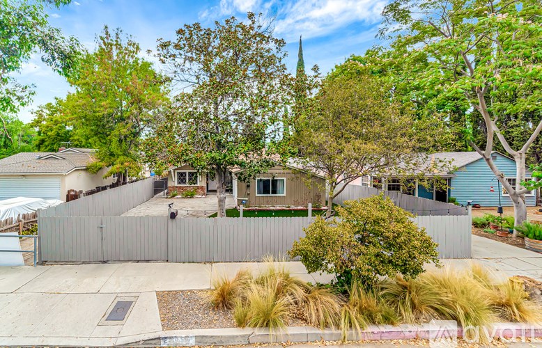 A house with a grey fence and a tree in front.