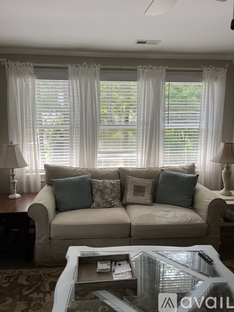 A living room with a couch, a coffee table, and a window with curtains.