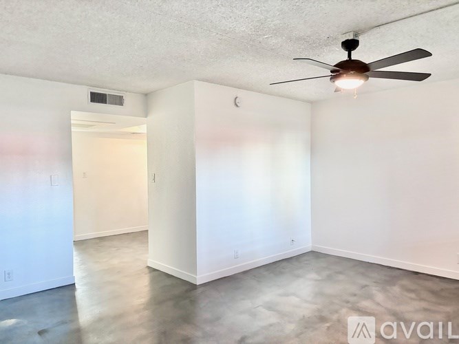 A spacious room with a ceiling fan and a doorway leading to another room.