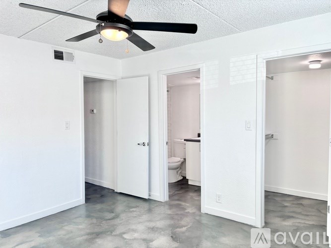 A room with a ceiling fan and a toilet in the background.
