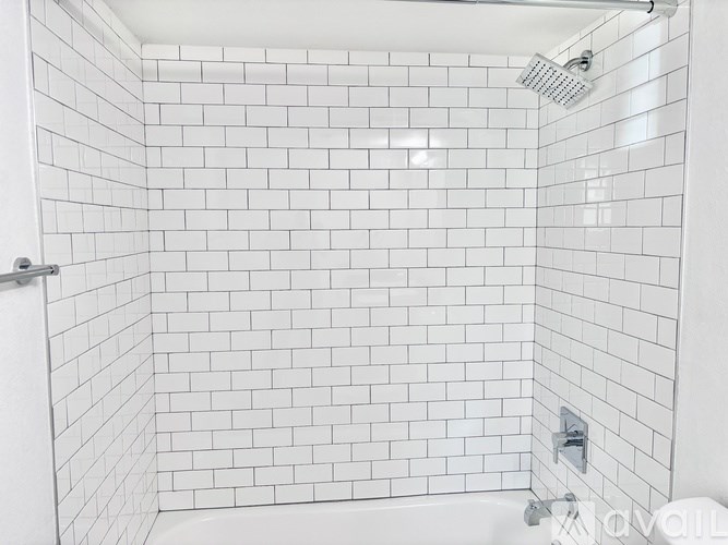 A white tiled shower stall with a shower head and faucet.