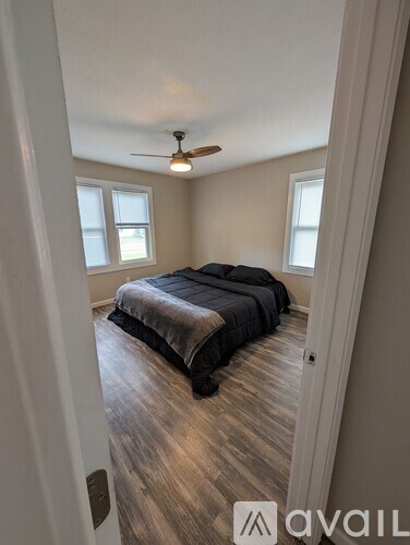 A bedroom with a bed, ceiling fan, and two windows.
