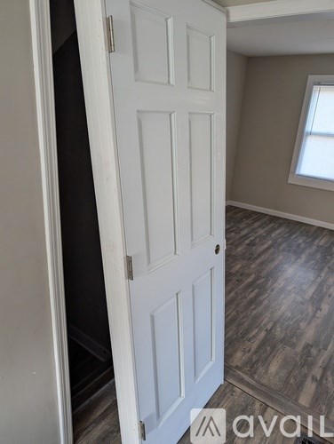 A white door is open to a room with wood flooring.