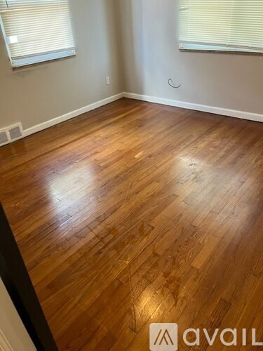 A room with wooden flooring and two windows.