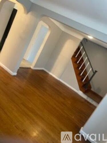 A wooden staircase with a metal railing is in the foreground of a room with white walls and wooden flooring.