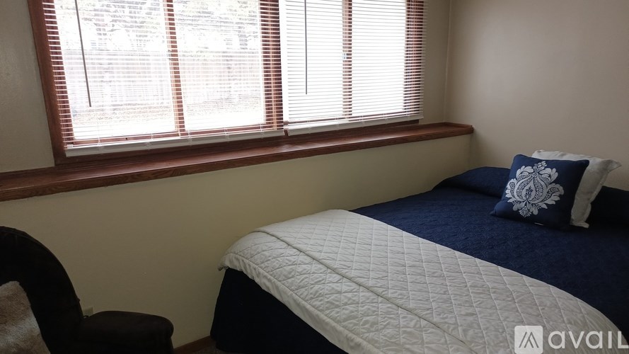 A bedroom with a bed, chair, and window with blinds.