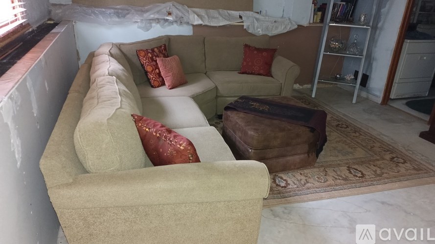 A beige couch with red pillows is in a room with a rug and a wooden ottoman.