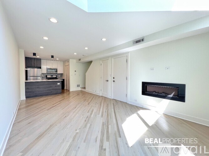 A spacious room with a fireplace and a kitchen area in the background.