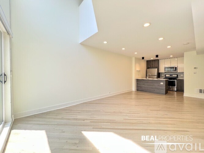 A spacious room with wooden flooring and a kitchen area in the background.