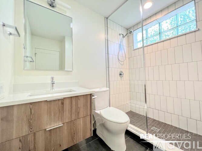 A white toilet sits in a bathroom with a wooden vanity and a large mirror.
