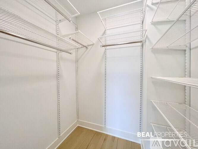 A white walk-in closet with shelves and a wooden floor.