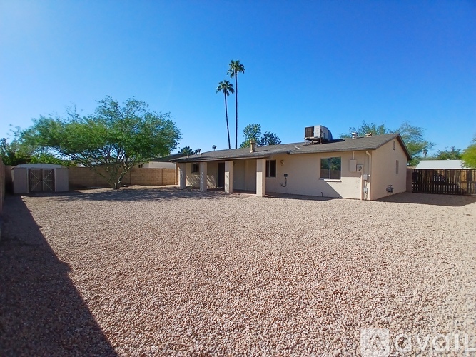 A house with a gravel driveway and palm trees in the background.