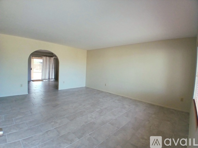 A spacious room with a grey floor and a window with curtains.