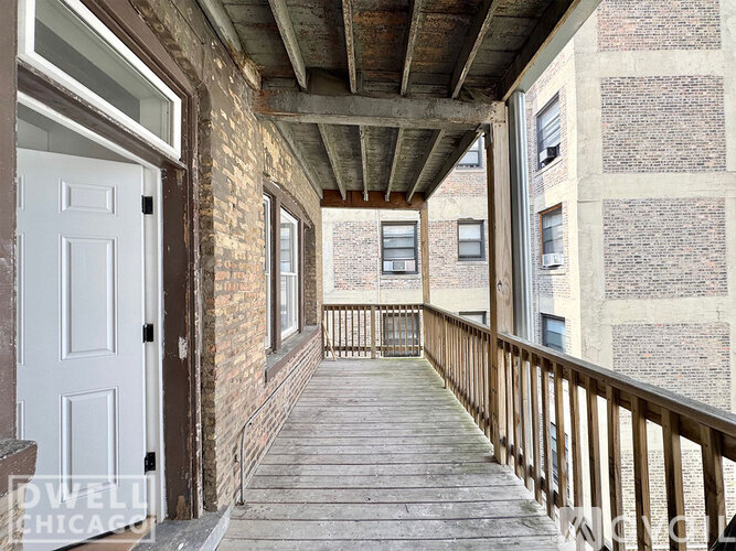 A wooden balcony with a white door and windows on a building.