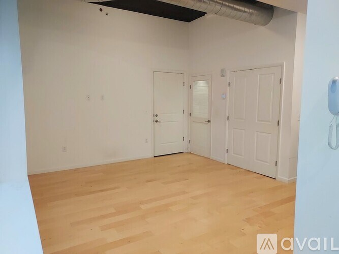 A room with wooden flooring and white walls, with two doors and a wall-mounted light fixture.