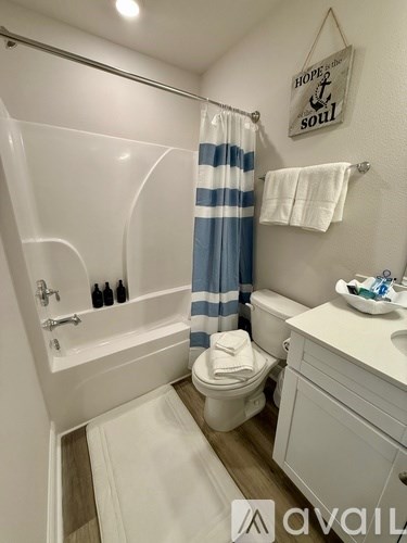 A bathroom with a white toilet, a white sink, a white bathtub with a blue and white striped shower curtain, a white towel, and a sign that says "Hope's Soul".