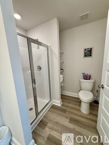A bathroom with a toilet, a glass shower door, and a framed picture on the wall.