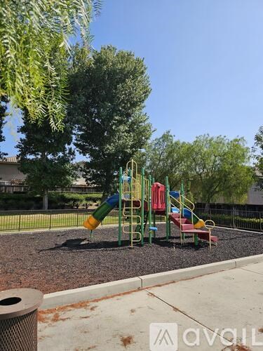 A playground with a slide, swings, and a tree.